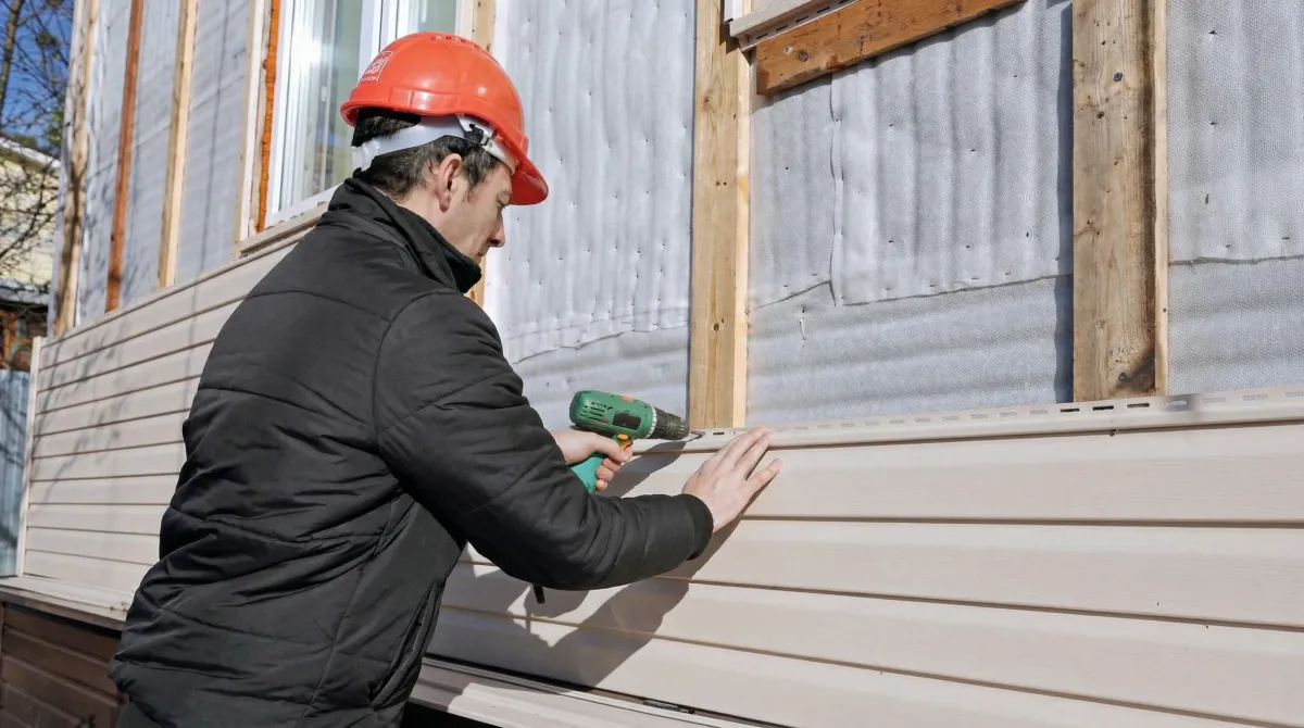 Siding replacement professional using a power drill to install new tan vinyl siding on a home exterior in Hialeah, FL